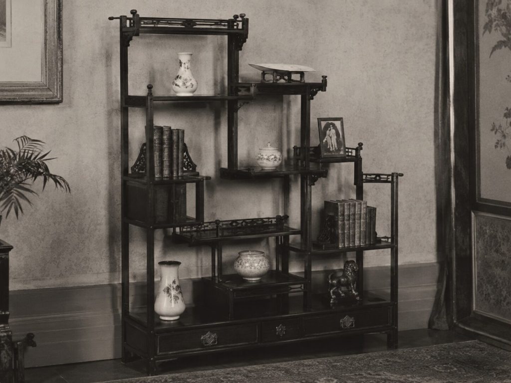 Illustration or period photograph of an asymmetrical Aesthetic Movement whatnot with ebonized wood, tier variation, and decorative geometry.